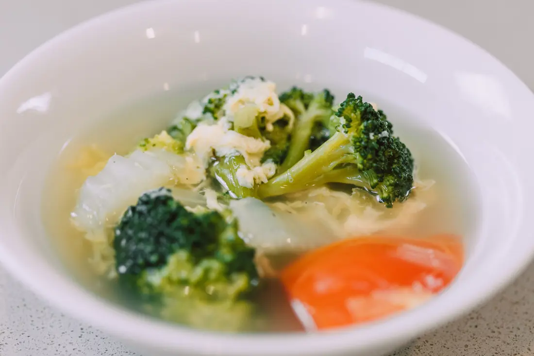 A bowl of soup with broccoli and carrot