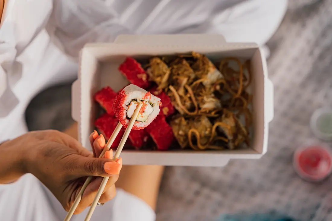 A takeaway box with noodles and a roll