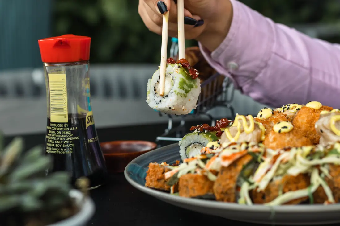 A piece of sushi held with chopsticks above a dish of soy sauce