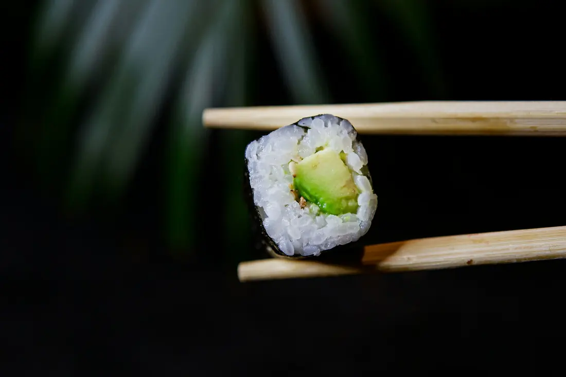 A single vegetable roll held in chopsticks