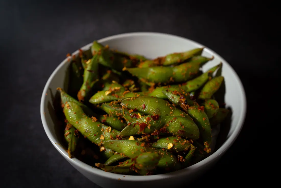 Edamame pods tossed with seasoning in a bowl