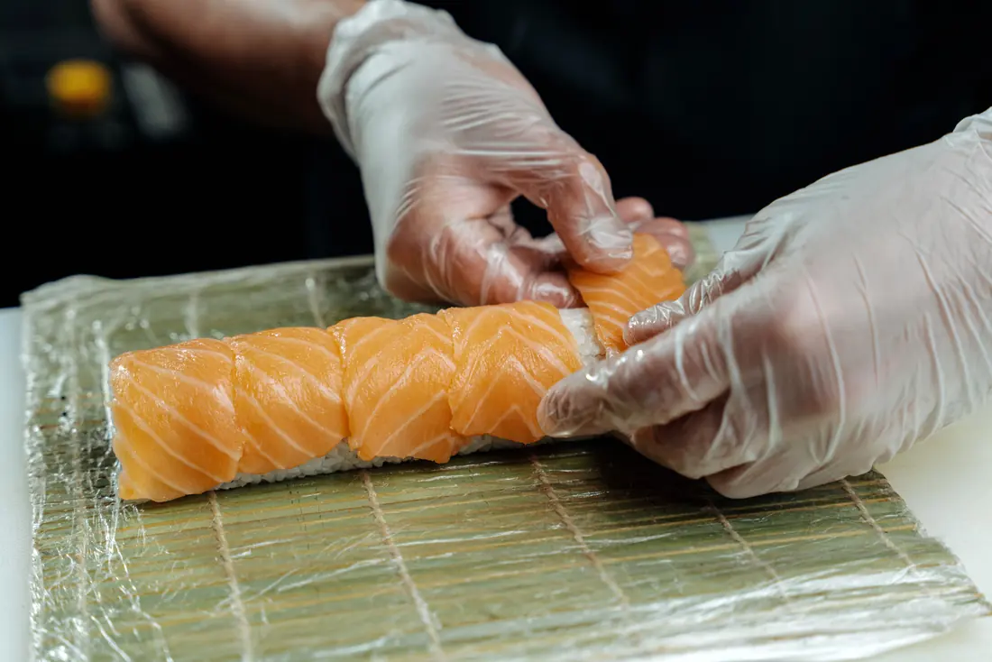 Gloved hands laying fish over a roll