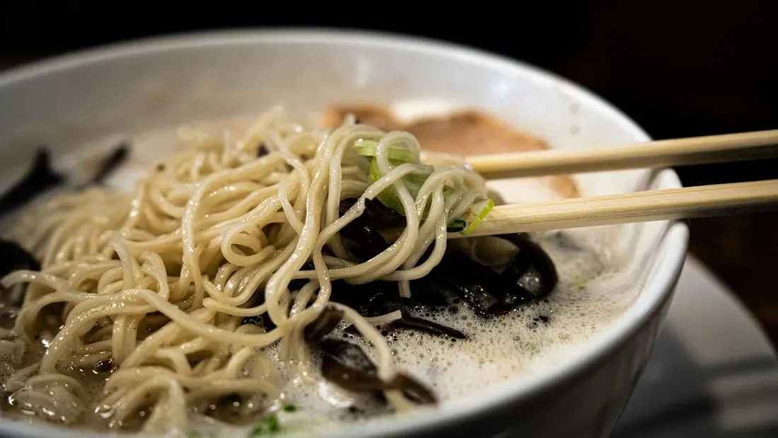 Noodles lifted from a bowl of hot broth with chopsticks