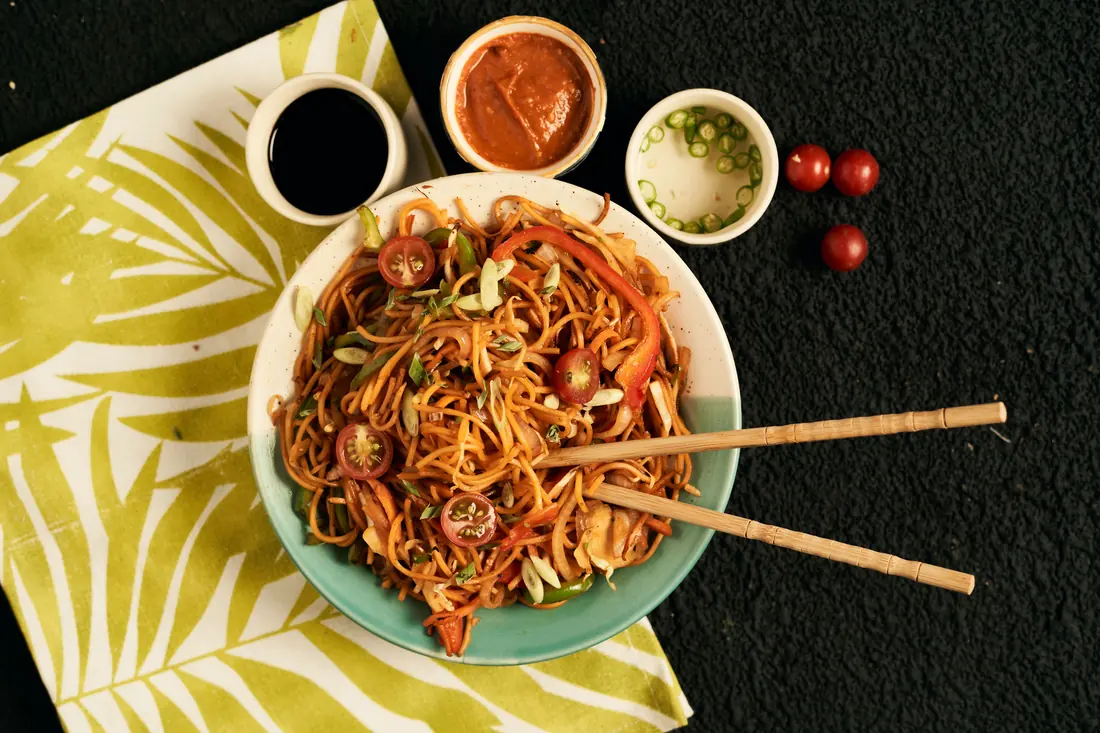 A bowl of sauced noodles with side dishes