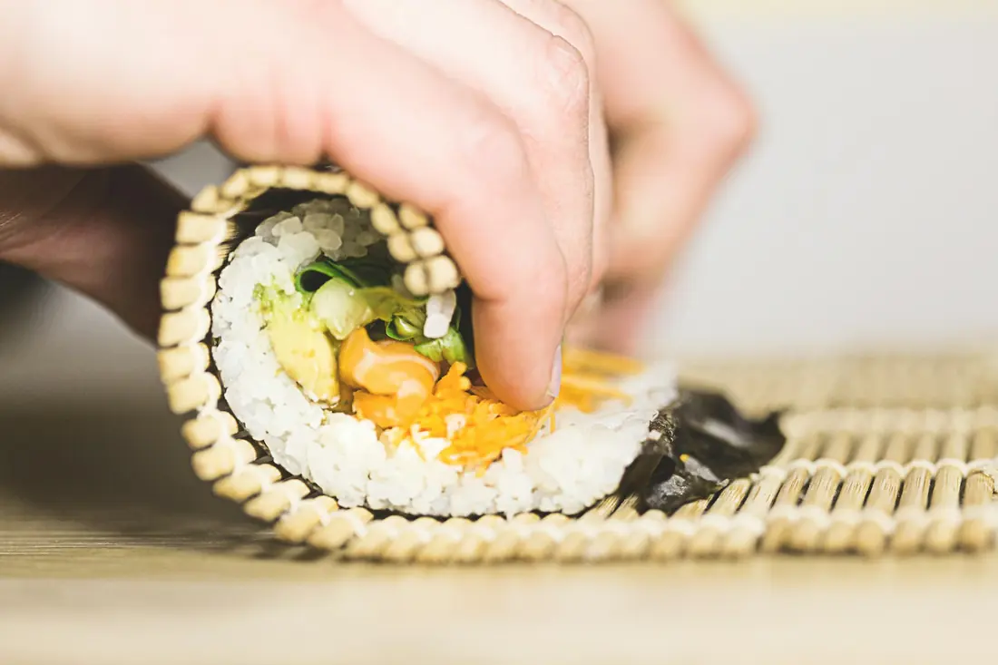 A sushi roll being assembled on a bamboo rolling mat