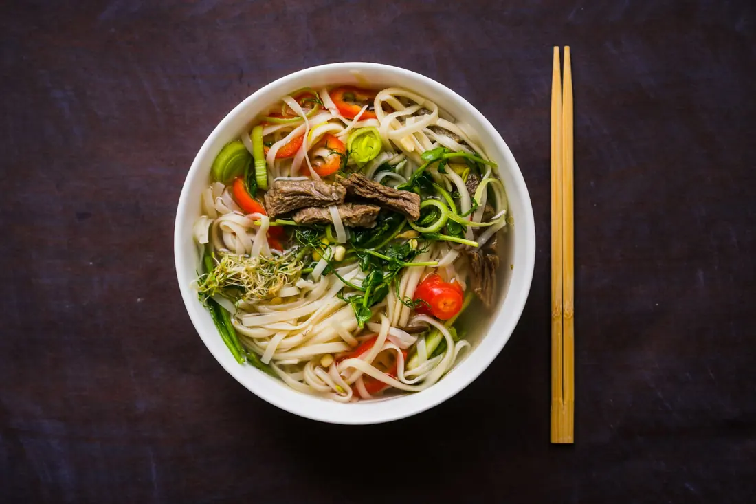 An overhead view of a pho bowl with chopsticks and a spoon
