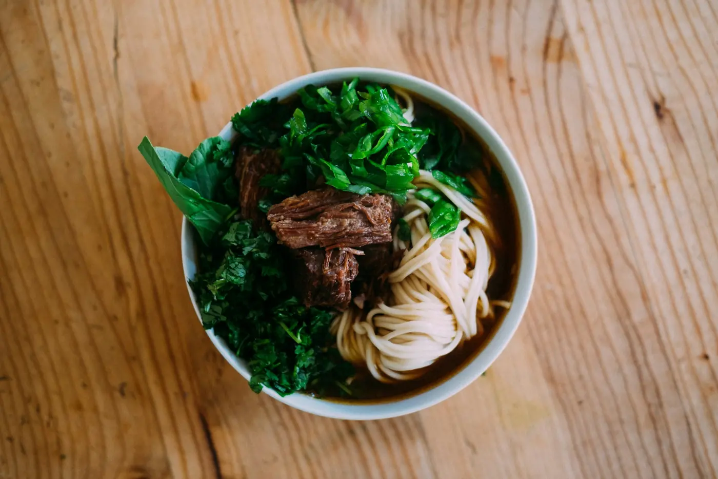 A steaming bowl of noodle soup topped with herbs and sliced meat