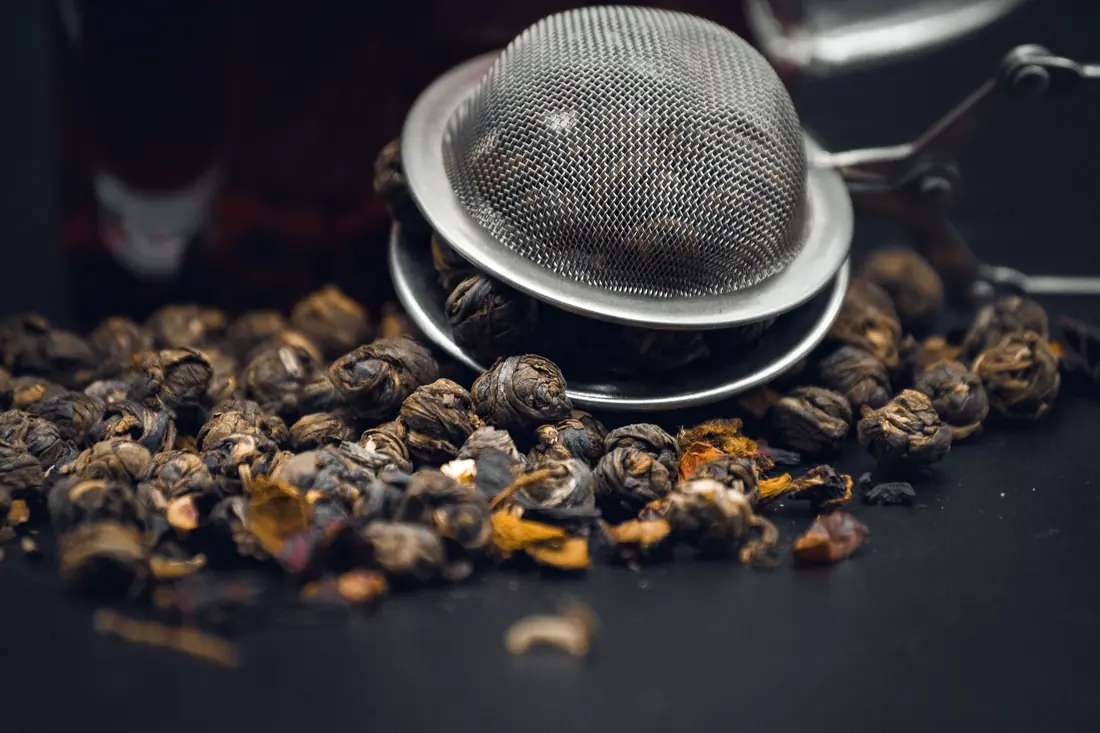 Rolled tea pearls beside a strainer