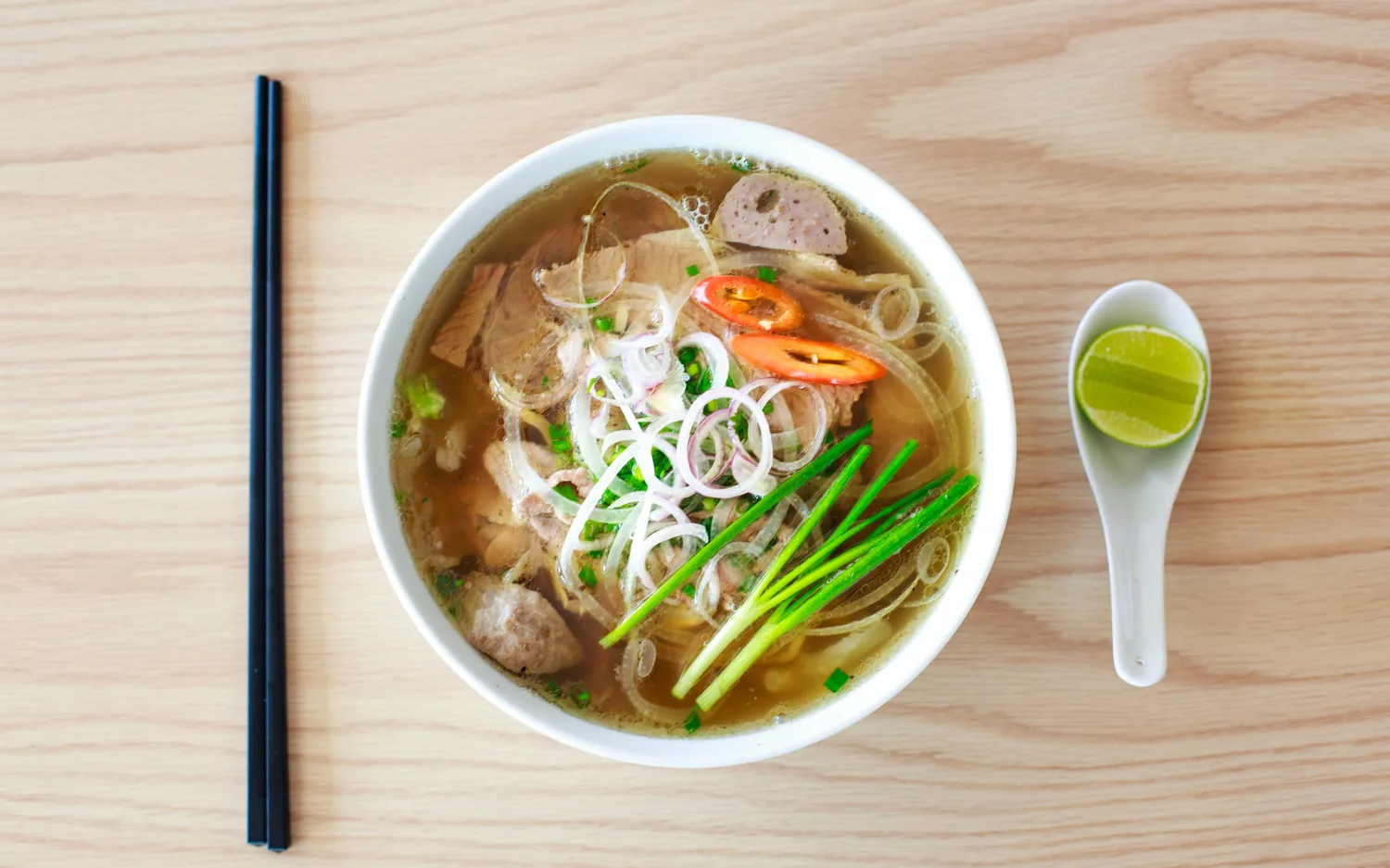 A bowl of noodle soup photographed from above on a pale wooden table