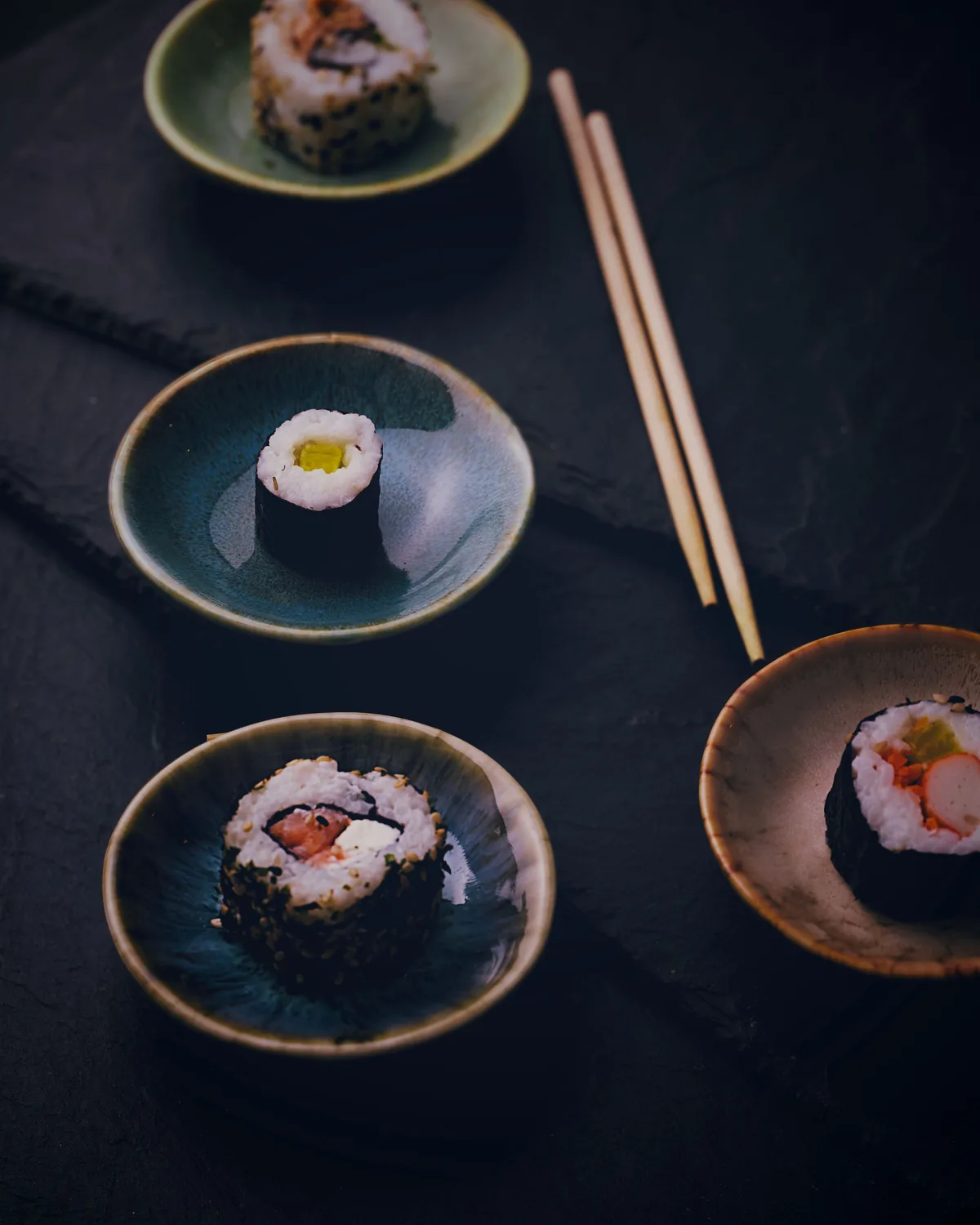 Sushi rolls served in small ceramic dishes on a dark slate surface
