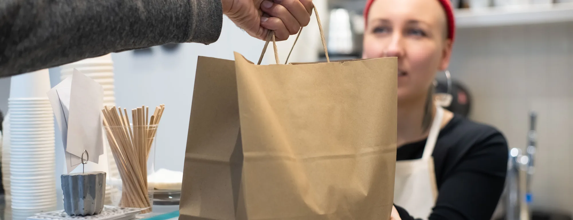 A paper takeaway bag being handed across a counter to a customer