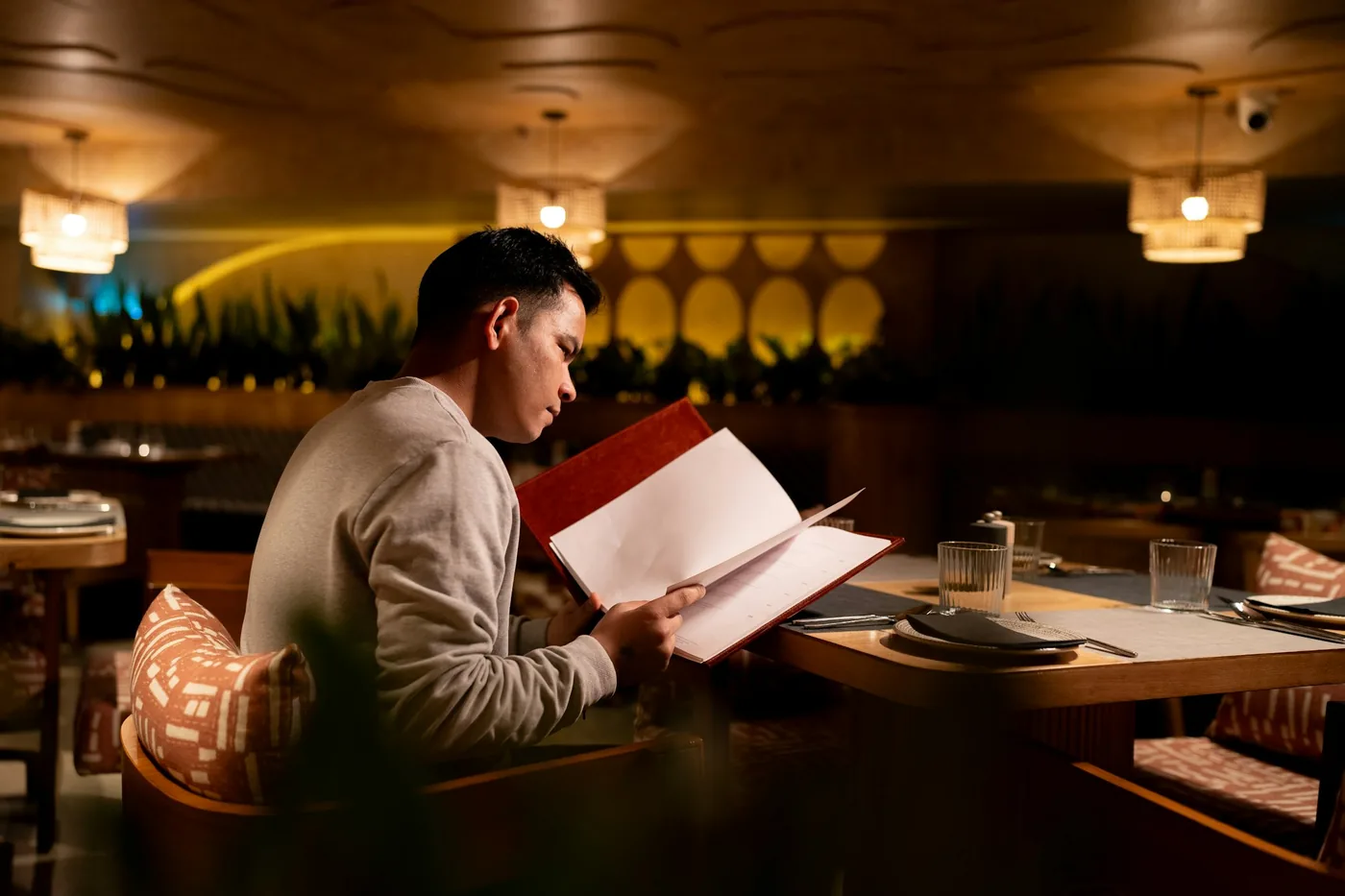 A guest reading a menu at a table in a warmly lit dining room