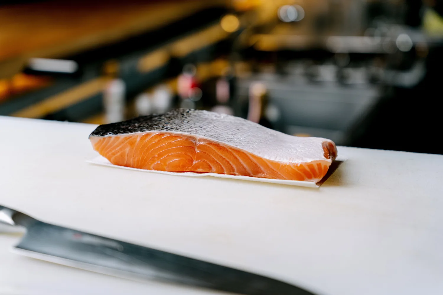 A salmon fillet on a white board with a knife laid in front of it