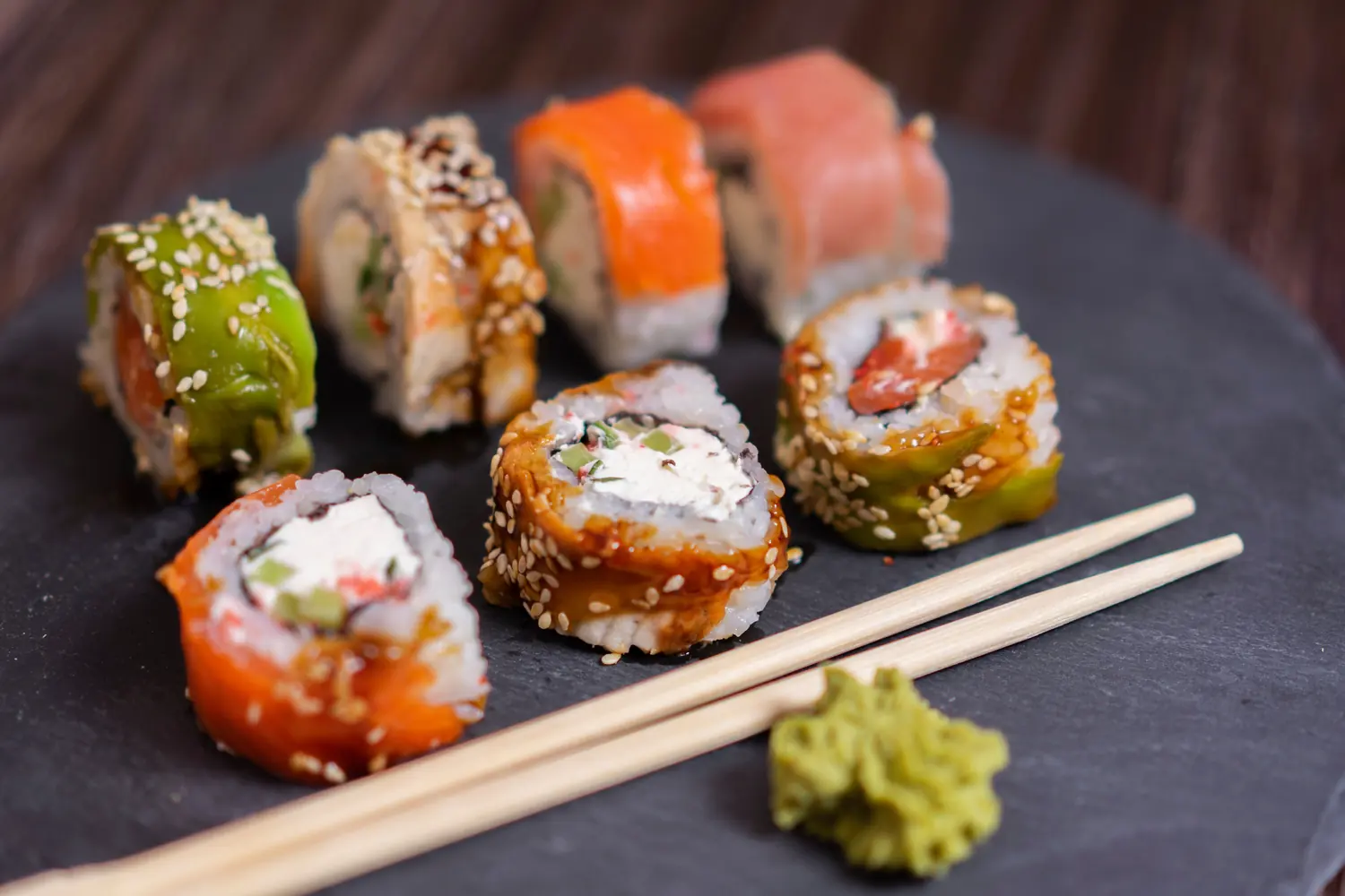 A platter of specialty sushi rolls arranged on a dark slate board
