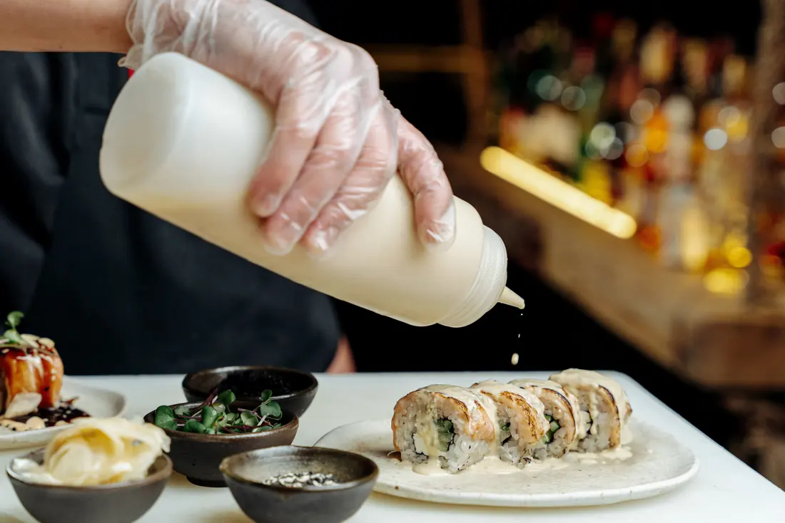 Sauce being squeezed over a roll from a bottle