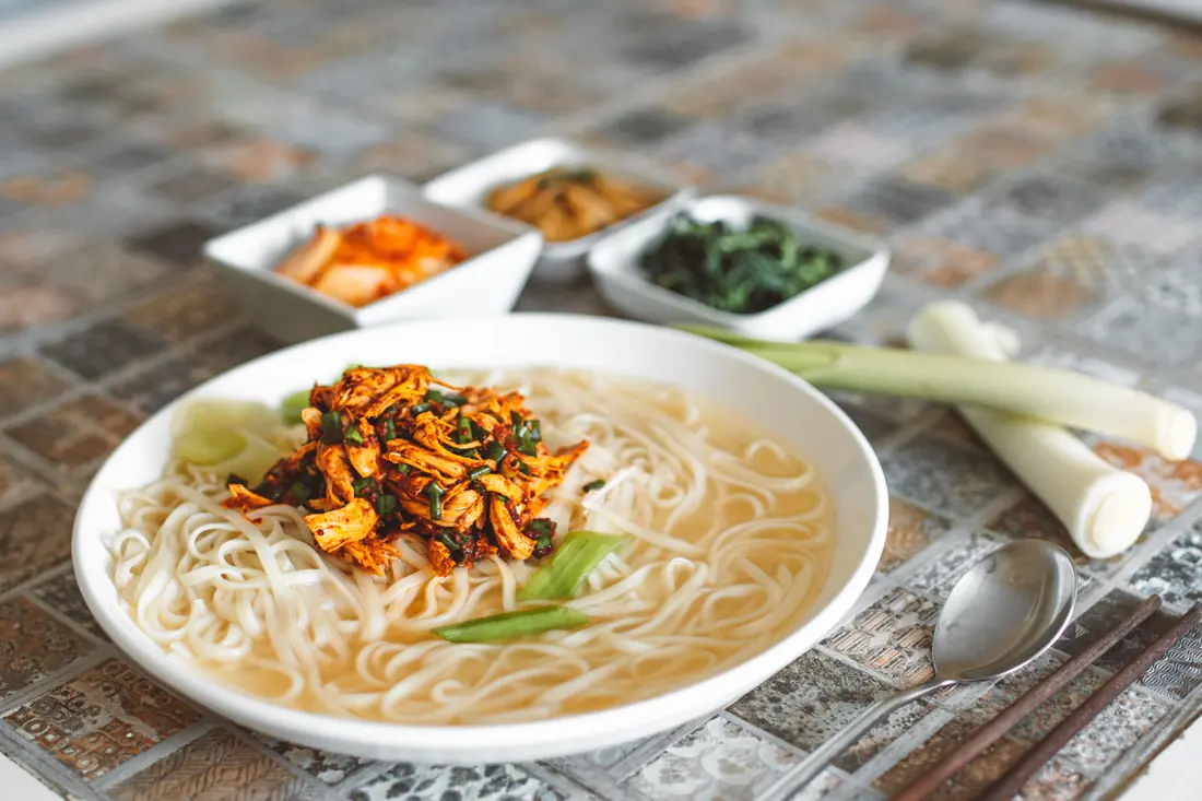A noodle soup topped with shredded chicken