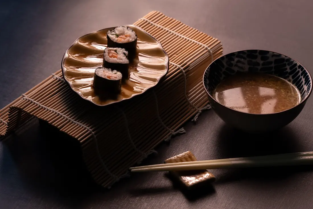 A small bowl of soup set beside a plate of sushi