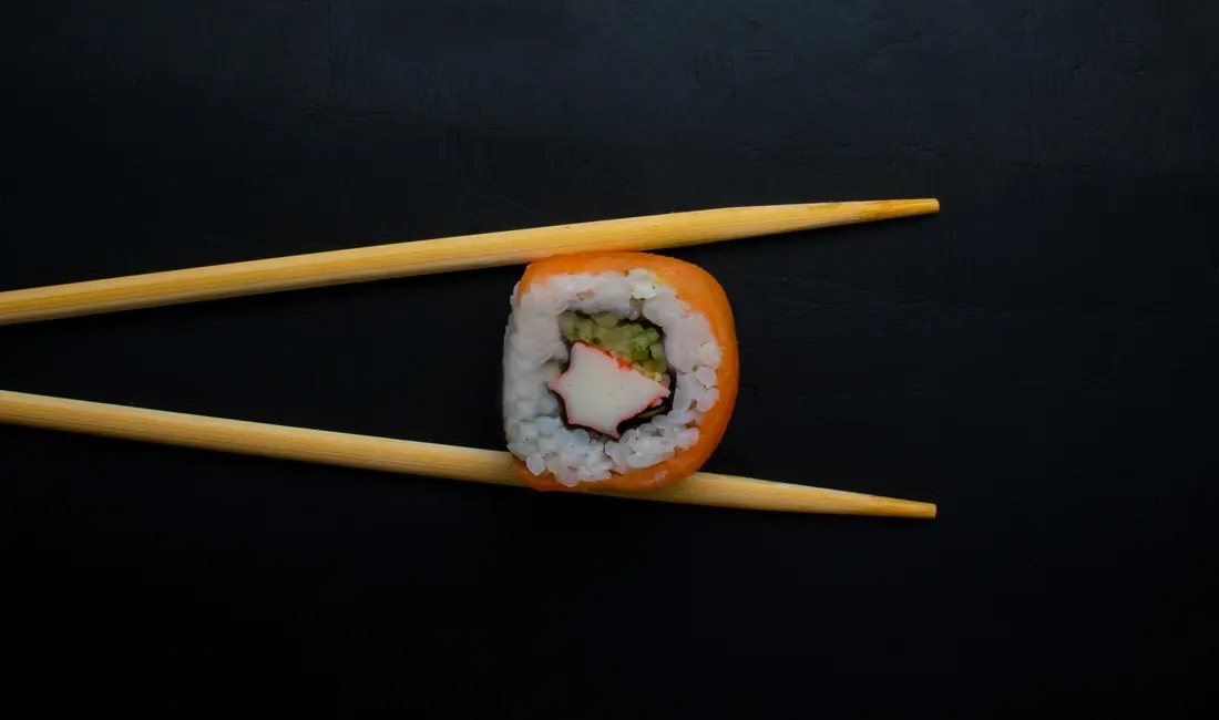 A single sushi roll piece lifted with chopsticks