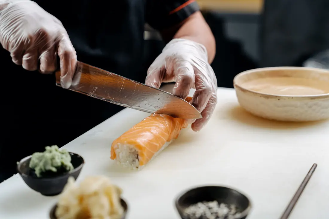 A chef slicing a finished sushi roll at the counter