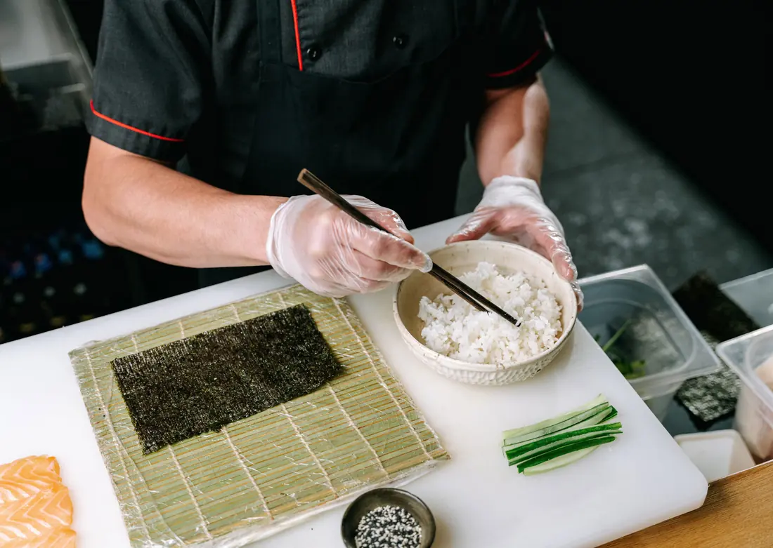 Sushi rice being spread across a sheet of nori