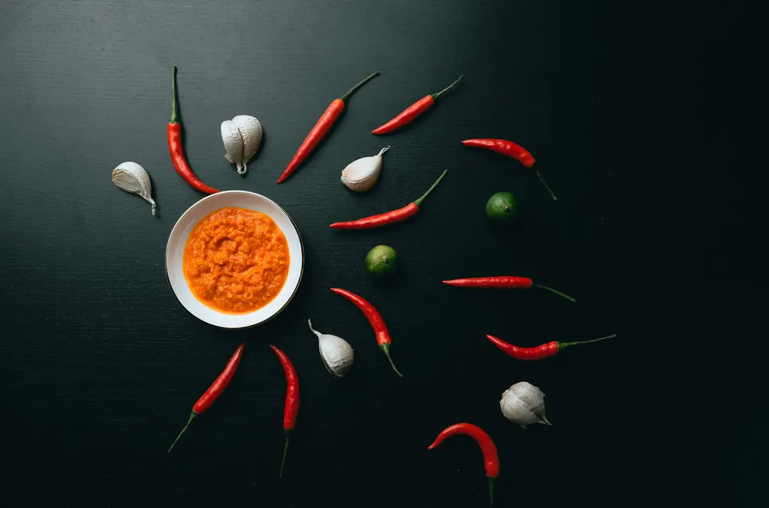 A dish of chilli dipping sauce surrounded by fresh chillies and garlic