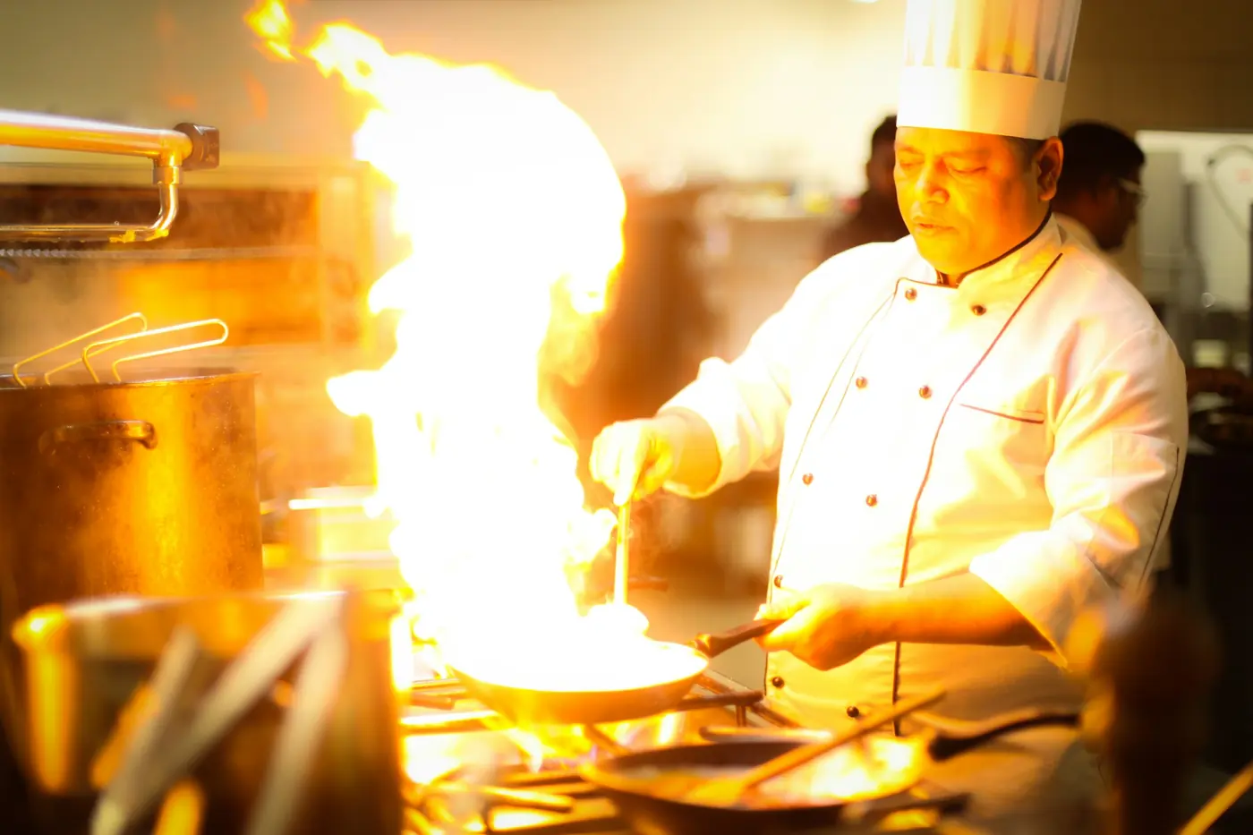 A chef cooking over high flames in a restaurant kitchen