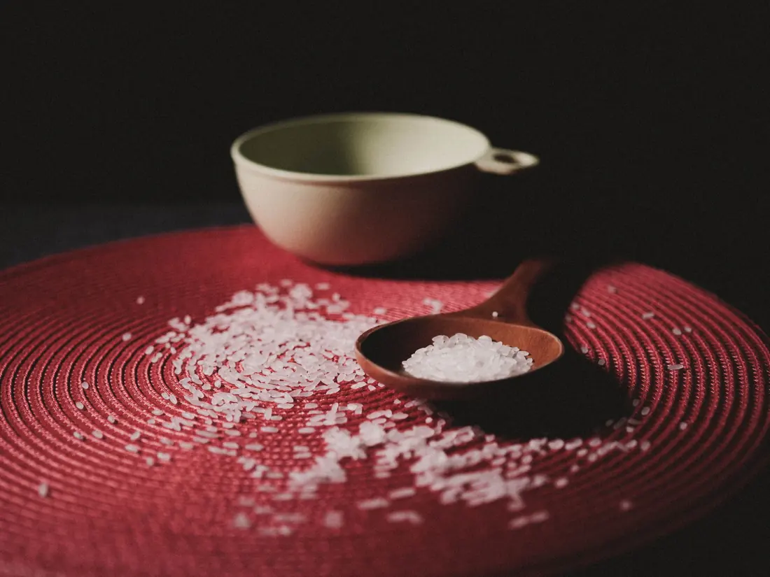 Uncooked rice grains beside a wooden spoon
