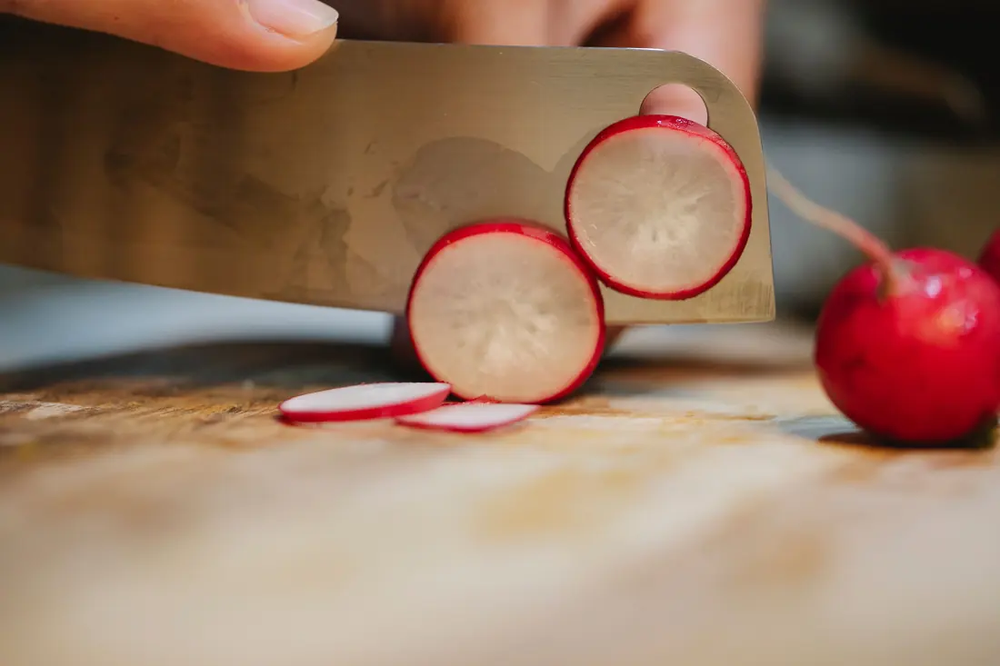 Small red radishes being sliced on a board